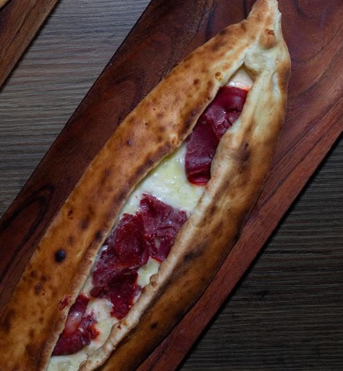 Boat-shaped stretch folded dough filled with akkawi cheese and Armenian basterma on a wooden board