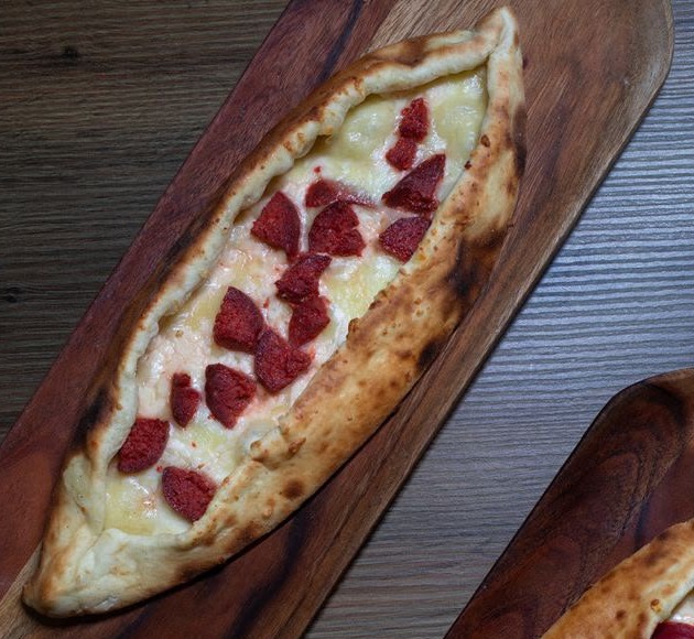 Boat-shaped stretch folded dough topped with Armenian sujuk and akkawi cheese on a wooden board